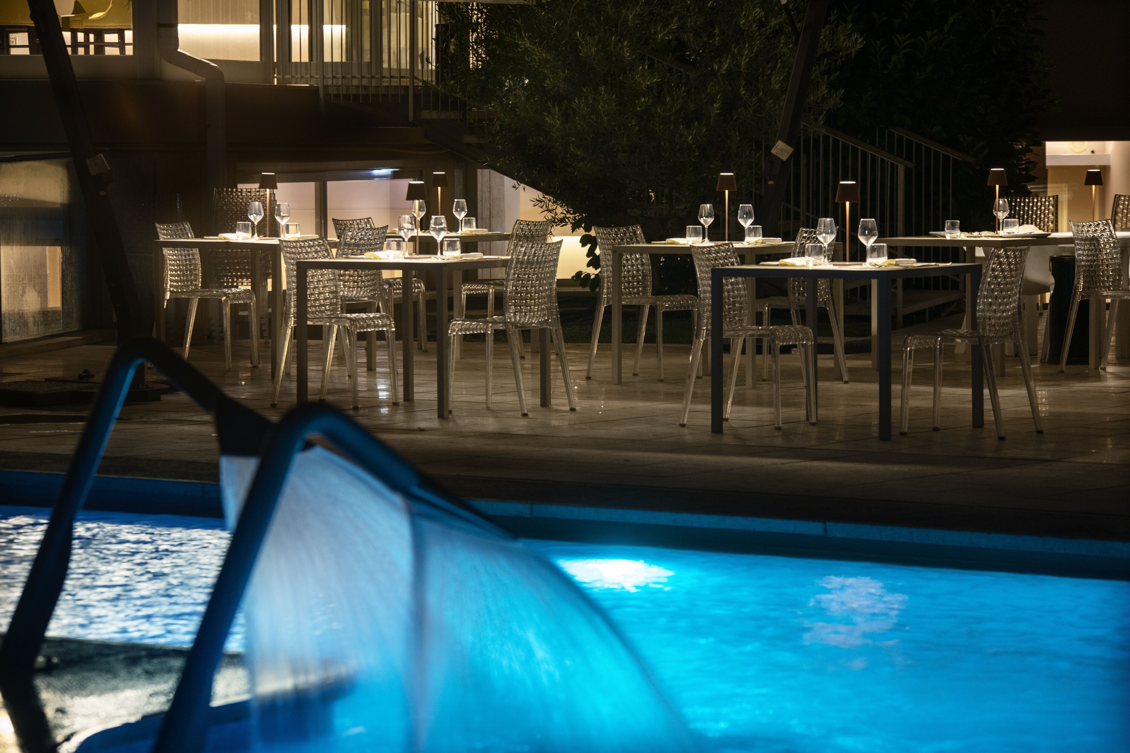An outdoor dining area with tables and chairs, a pool, and a staircase leading to an upper level.
