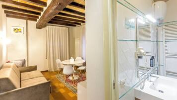A room with a wooden ceiling, a dining table with chairs, a sofa, and a patterned rug.