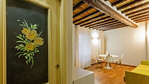 A room with a wooden ceiling, a dining area with a table and chairs, and a yellow sofa.