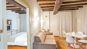 A cozy room with a bed, a sofa, a dining table with chairs, and a small kitchen area.