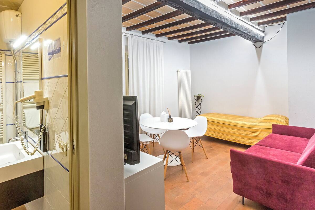 Una habitación de hotel con baño, una zona de comedor con mesa y sillas, y un rincón de estar con sofá.