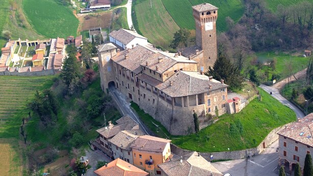 An aerial view of a historic town with a prominent tower, narrow streets, and surrounding green fields.