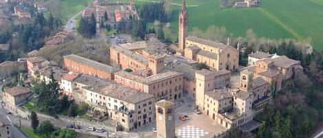 An aerial view of a historic town with a prominent church, a central square with a checkered pavement, and surrounding green fields.