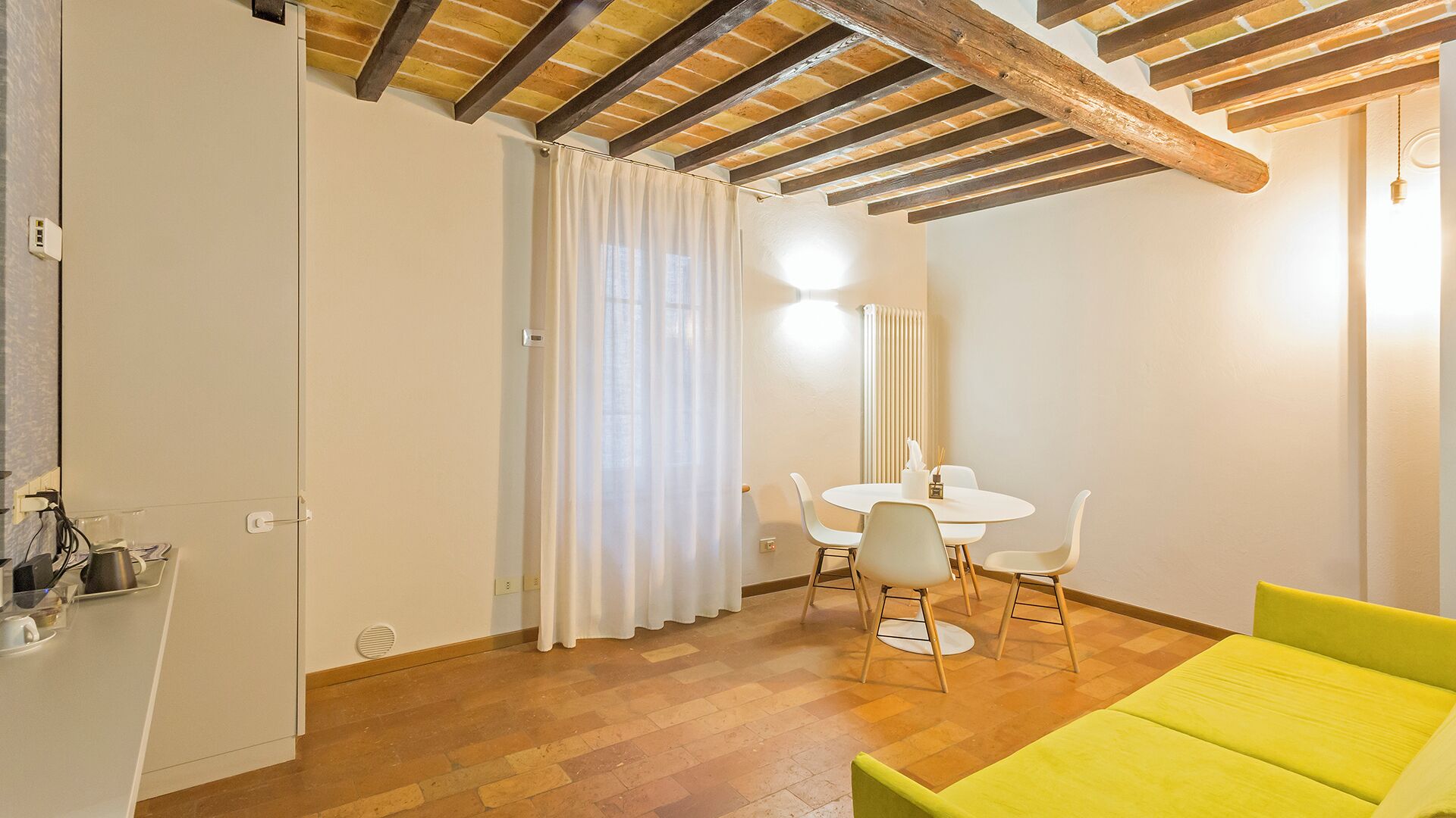 A dining area with a round table and four chairs, a yellow sofa, and a wooden ceiling.