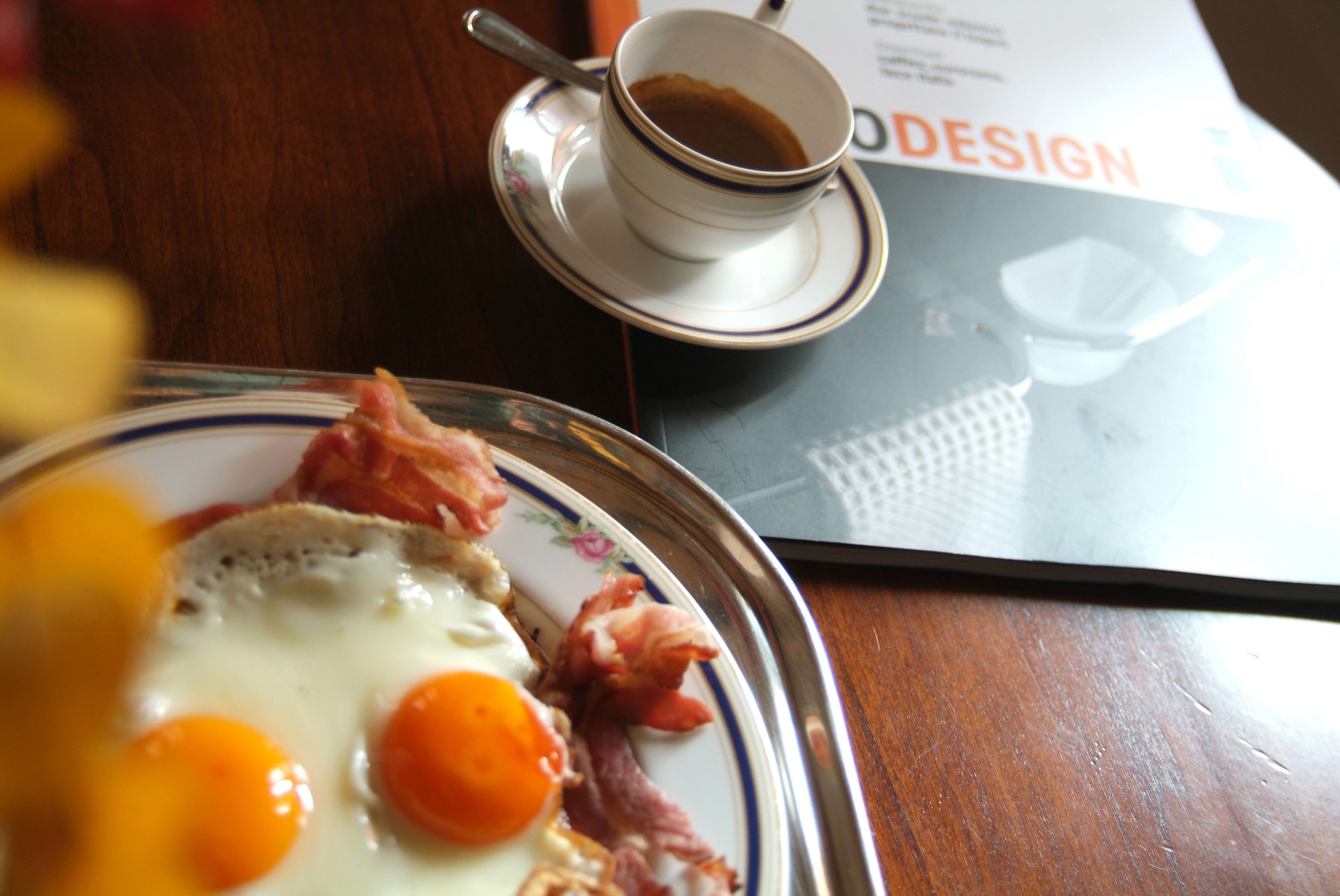 A breakfast plate with eggs and bacon, a cup of coffee, and a magazine on a table.