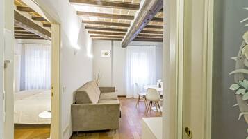 Una sala de estar moderna con un sofá color beige, una mesa de comedor con sillas y una cocina visible a través de un umbral abierto.