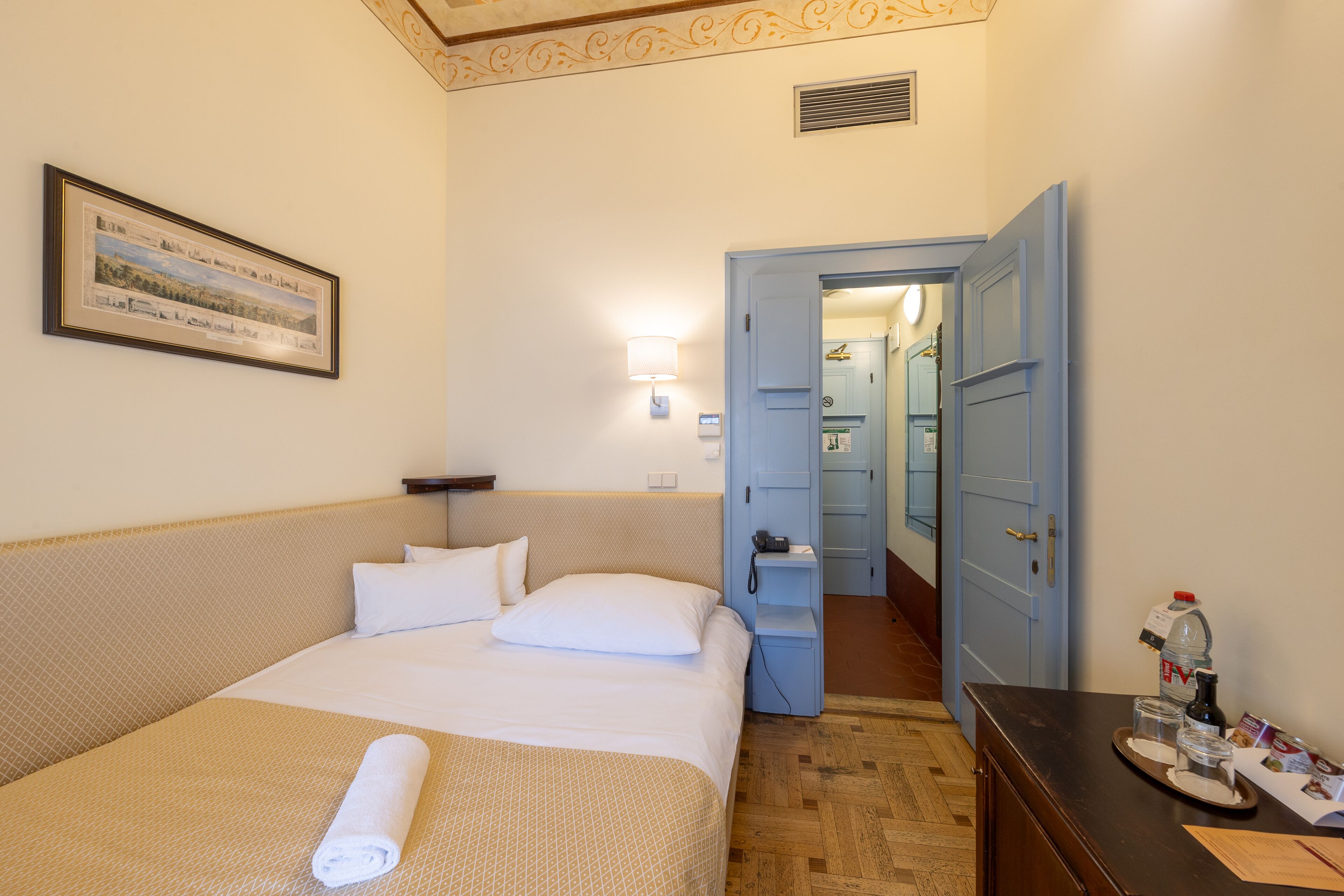 Una camera d'albergo con un letto rifatto, un quadro appeso alla parete, un comodino con una lampada e una porta che dà accesso al bagno.