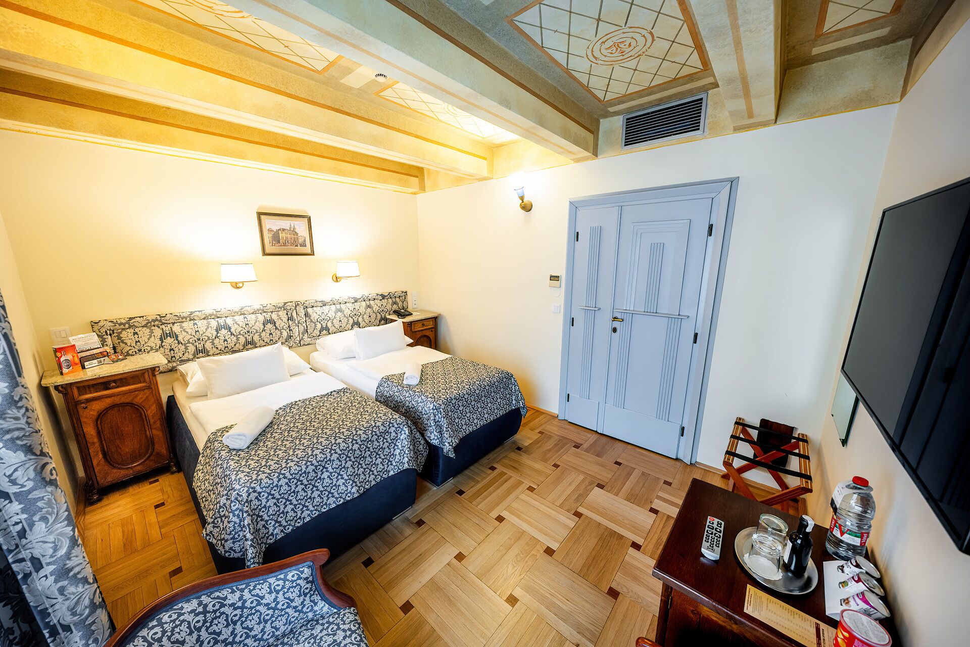 Habitación de hotel con dos camas, suelo de madera, televisor y escritorio con silla.