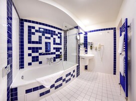 Casa de banho com banheira, chuveiro e lavatório, com azulejos azuis e brancos.