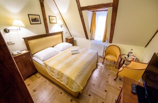 Quarto com uma cama grande, mesa de cabeceira de madeira, uma cadeira, uma mesinha com um controle remoto e uma janela com cortinas.