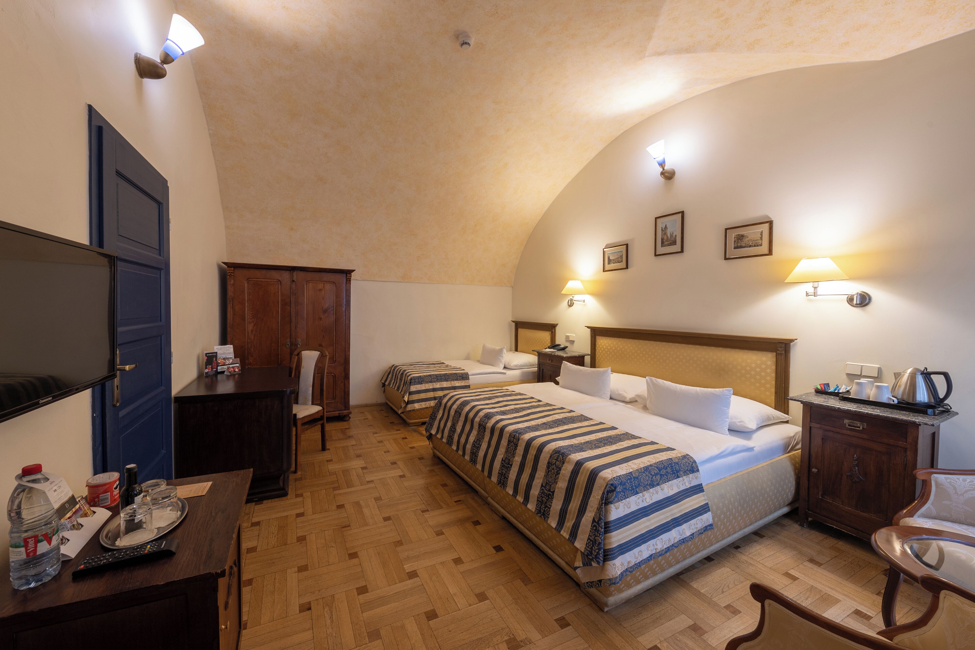 Une chambre d’hôtel avec deux lits, un bureau avec une télévision, une armoire en bois et un petit meuble avec une bouilloire.