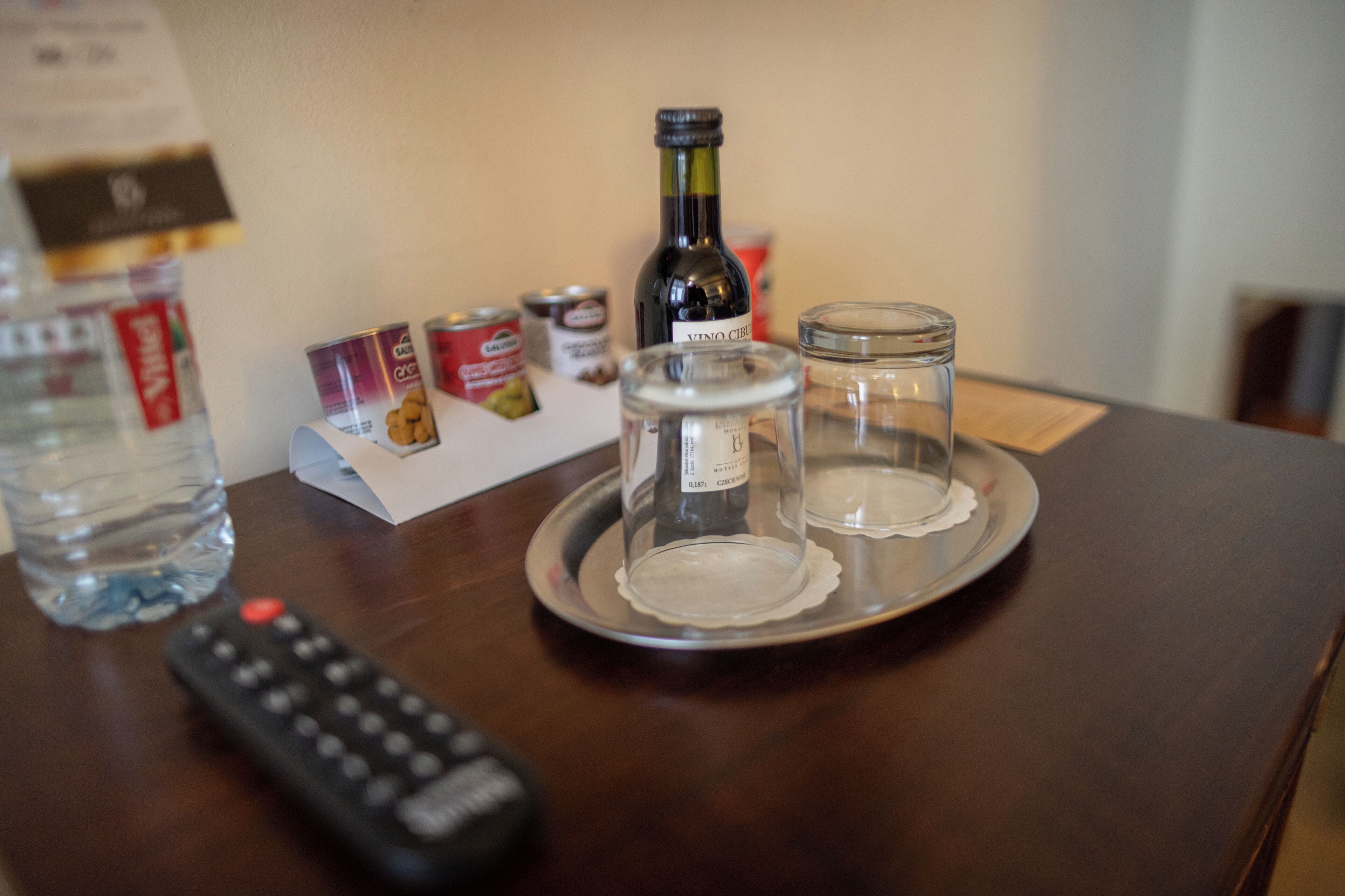 Ein Tablett mit einer Flasche Vino Cielo Wein, zwei leere Gläsern, einer Wasserflasche und einer Fernbedienung auf einer Holztischplatte.