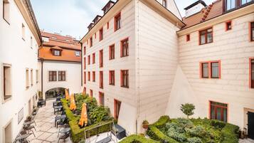 A courtyard with outdoor seating, a small garden, and a building with multiple windows and balconies.