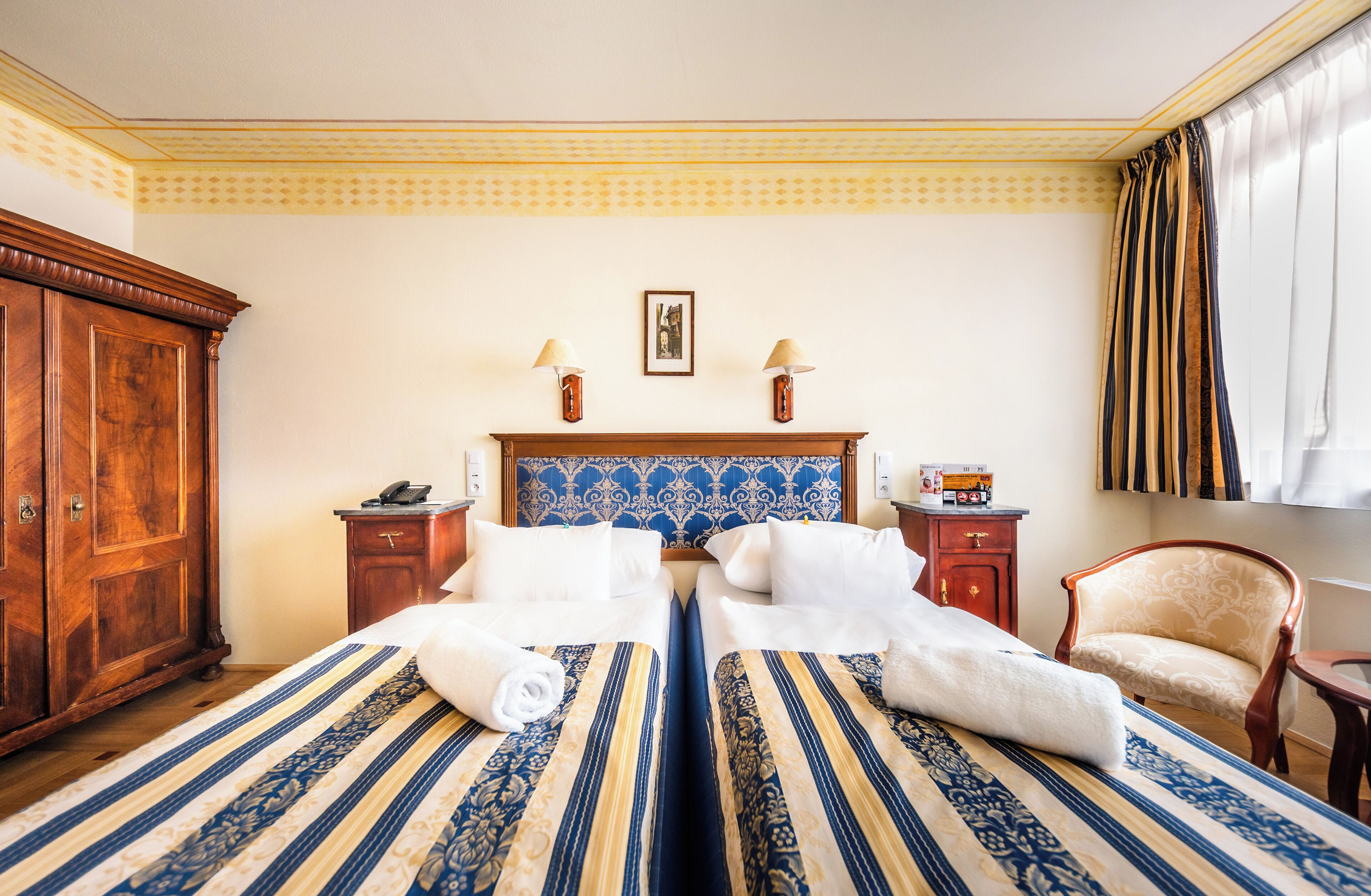 Une chambre d’hôtel avec un grand lit, deux tables de chevet, une armoire en bois, une chaise et une fenêtre avec des rideaux.