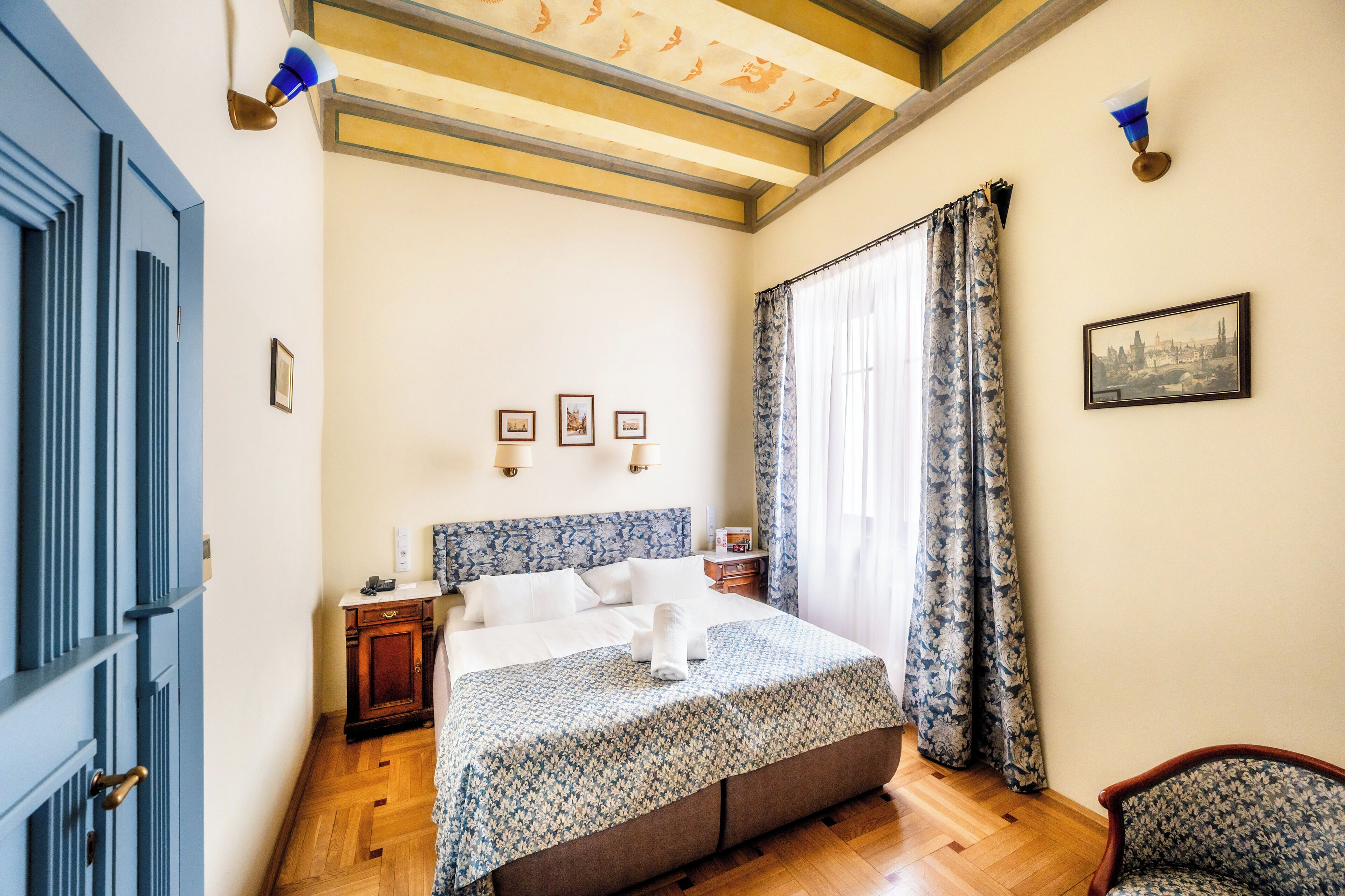 A bedroom with a bed, a nightstand, a chair, a window with curtains, and a framed picture on the wall.