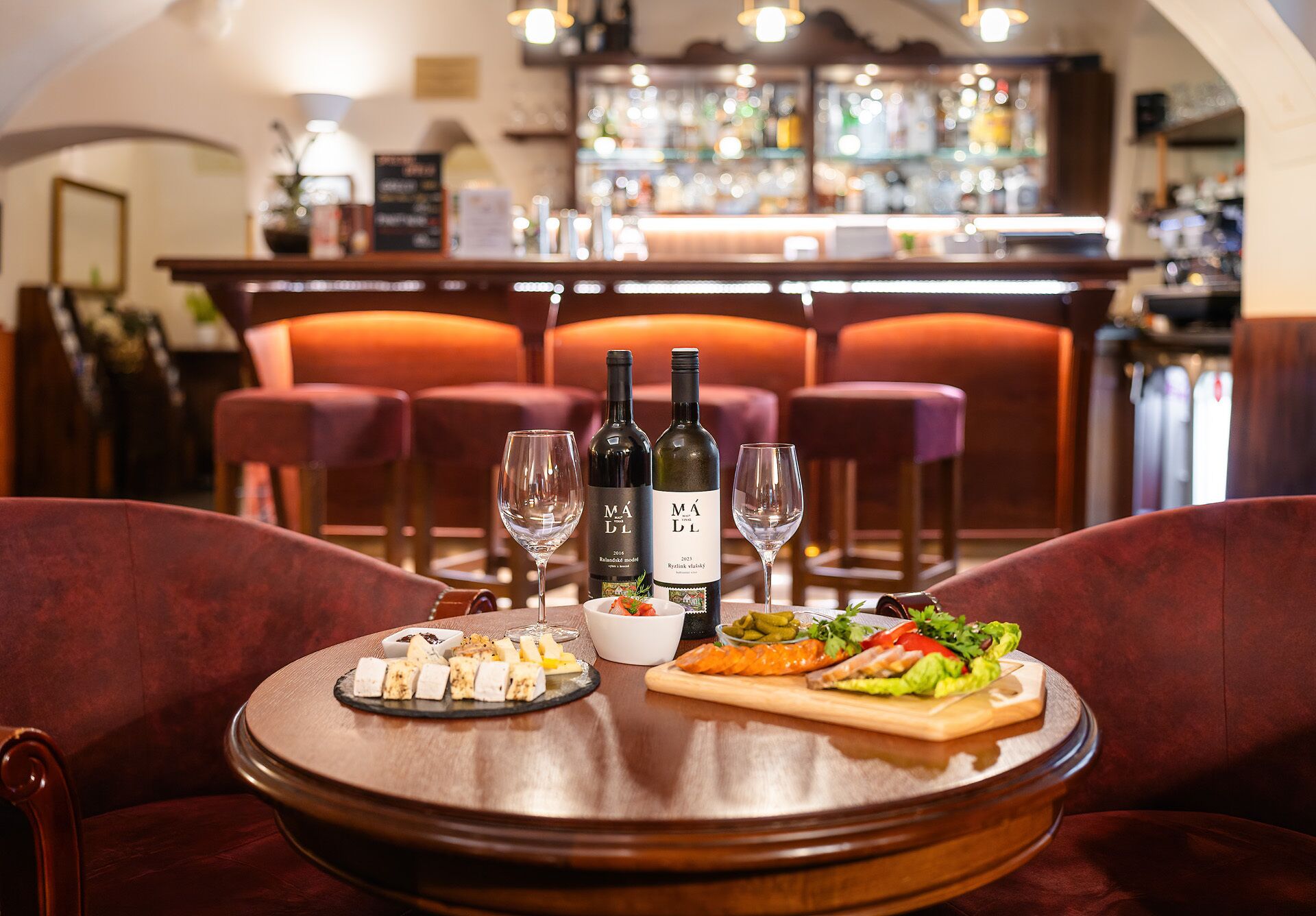 En bar med to flasker vin, to glas, et bord med mad og en vandflaske.