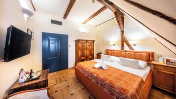 A bedroom with a wooden ceiling, a bed with an orange bedspread, a TV, a desk with a bottle, and a blue door.