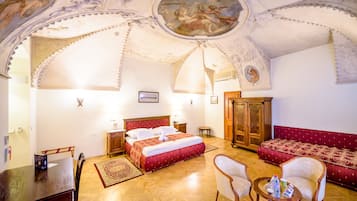 Quarto de hotel com uma cama grande, um guarda-roupa de madeira, um sofá vermelho, uma mesa de jantar e um candelabro.