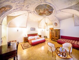 Quarto de hotel com uma cama grande, um guarda-roupa de madeira, um sofá vermelho, uma mesa de jantar e um candelabro.