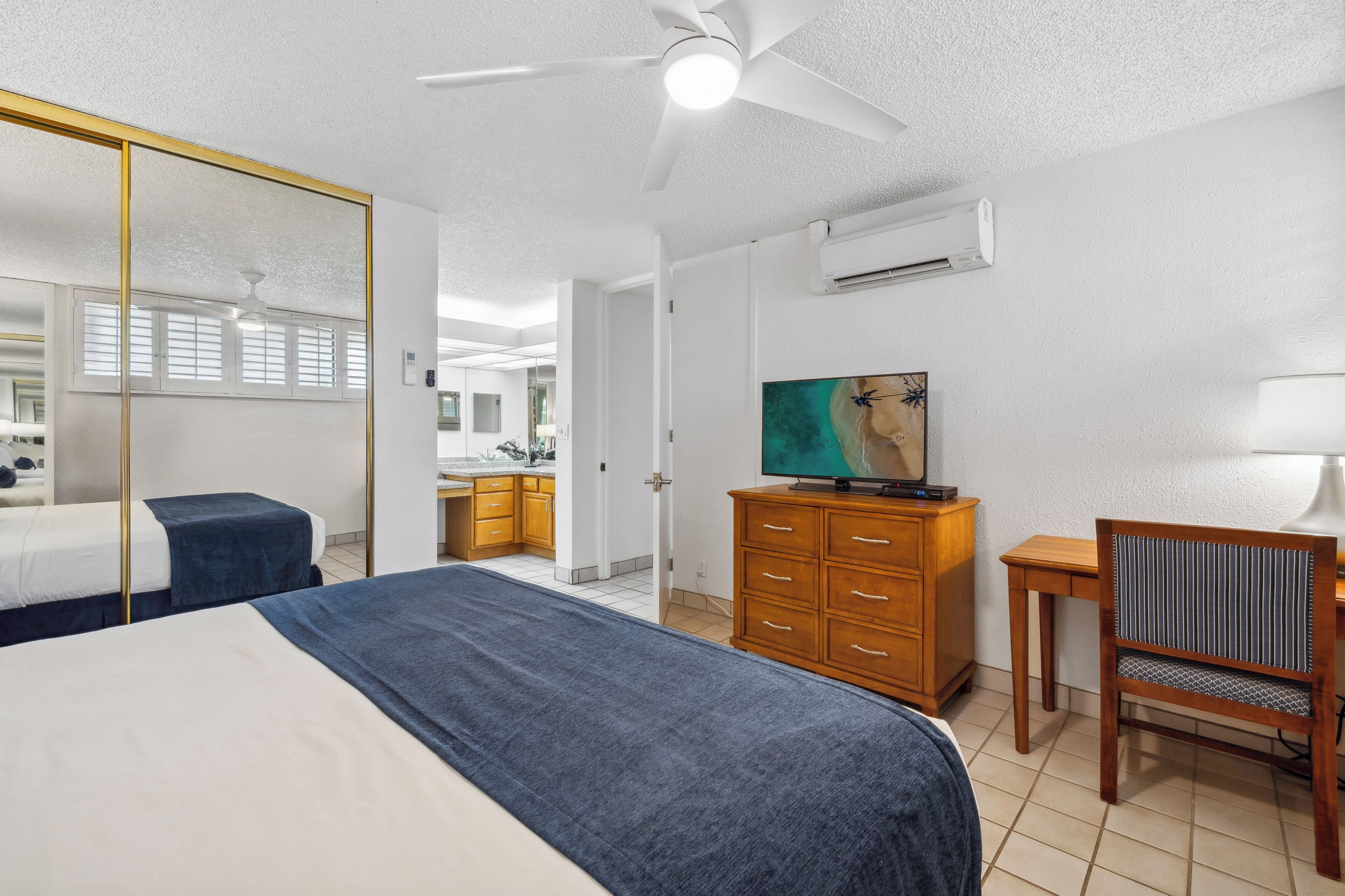 A hotel room with a bed, a desk, a chair, a television, a wardrobe, and a mirror.