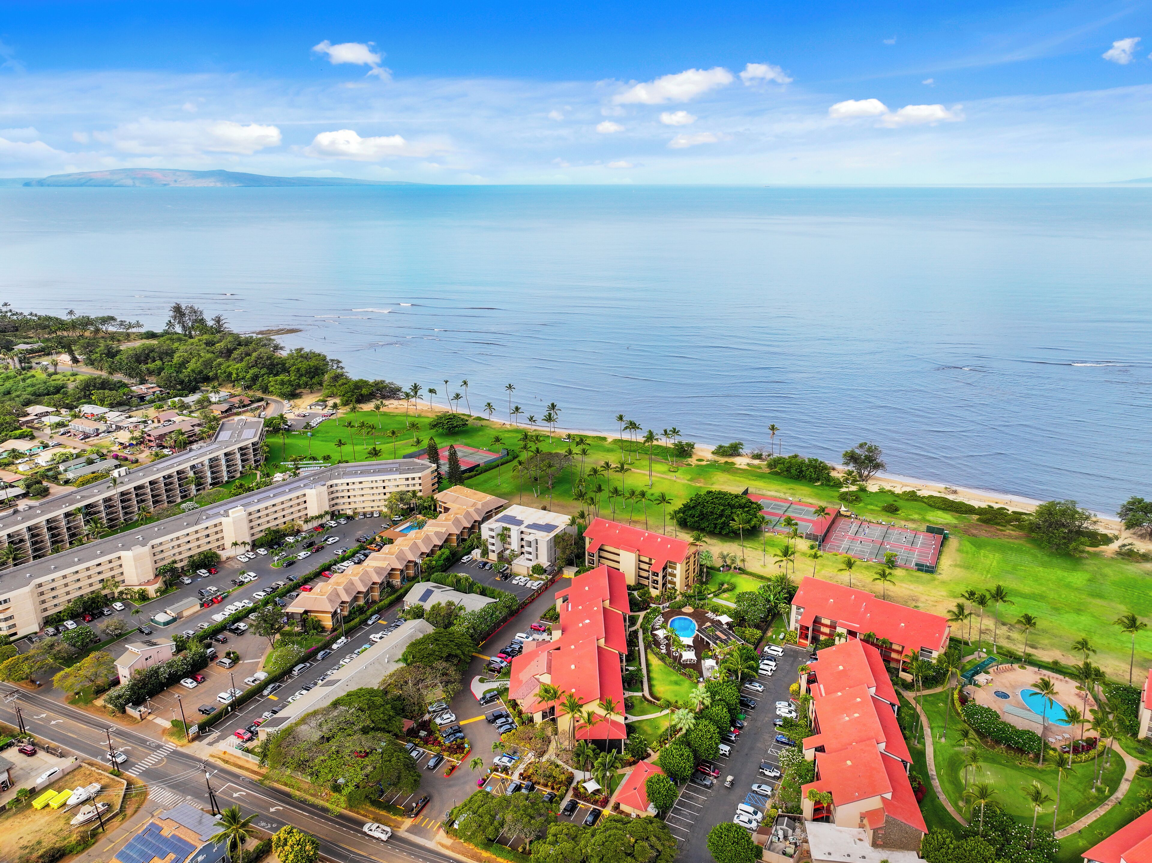 Un resort con varias construcciones, un estacionamiento y una zona de playa con palmeras.