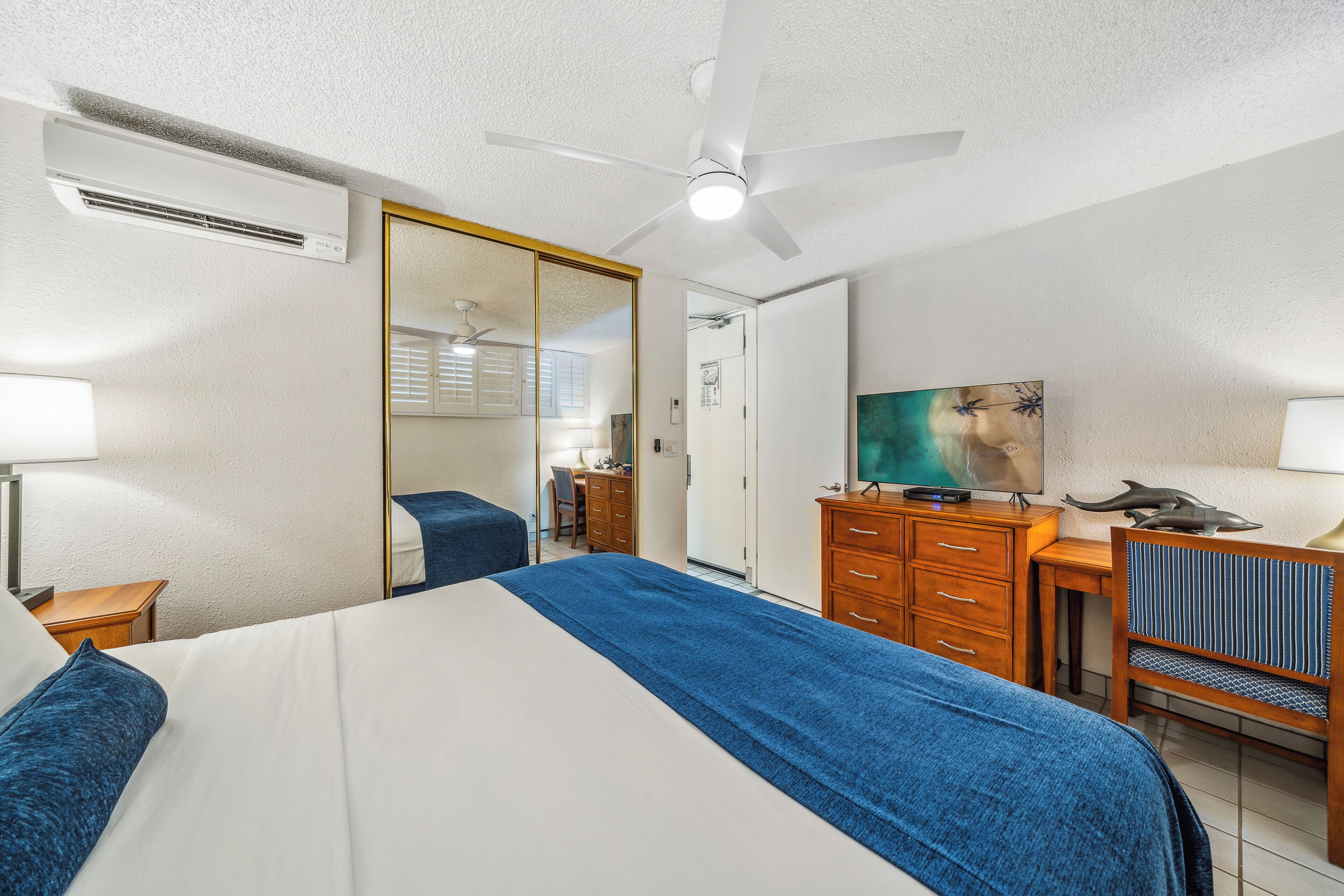 A hotel room with a bed, a desk, a chair, a TV, and a ceiling fan.