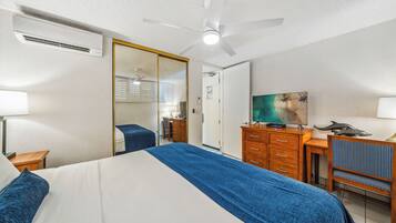 A hotel room with a bed, a desk, a chair, a TV, and a ceiling fan.