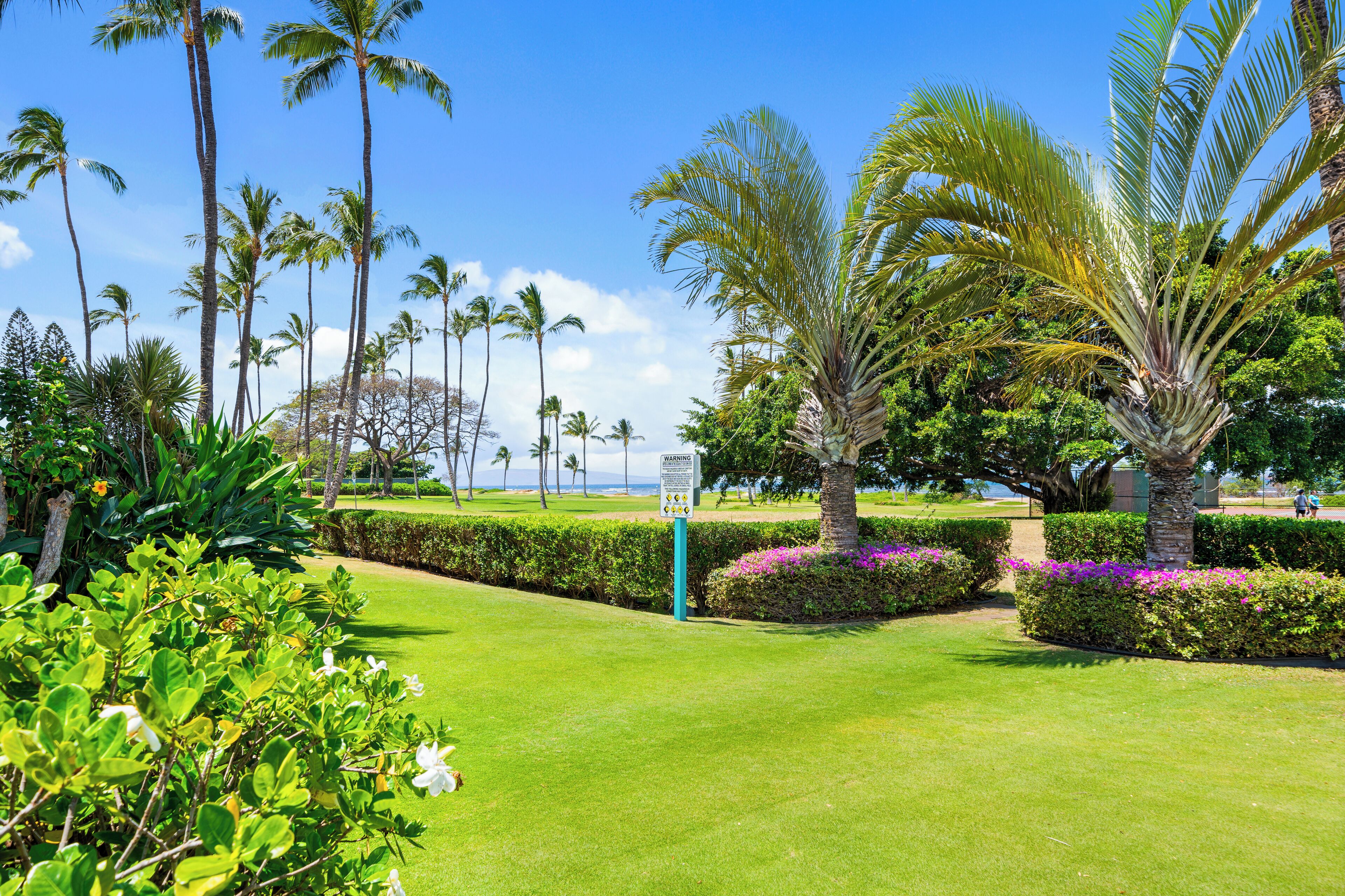 A well-maintained garden with palm trees, manicured lawns, and a signpost.