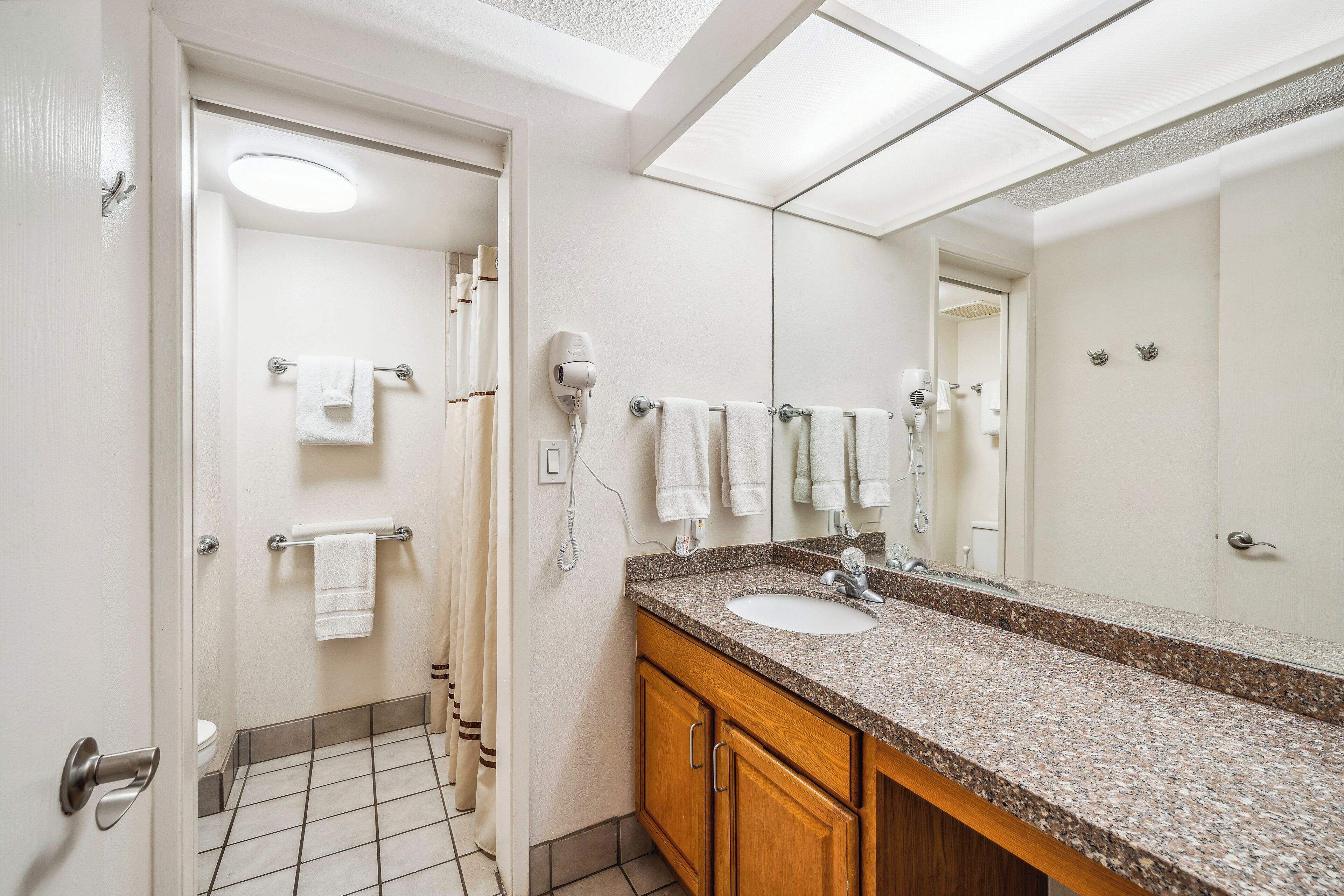 Un baño moderno con lavabo de granito, un espejo grande y una zona de ducha con puerta de cristal.
