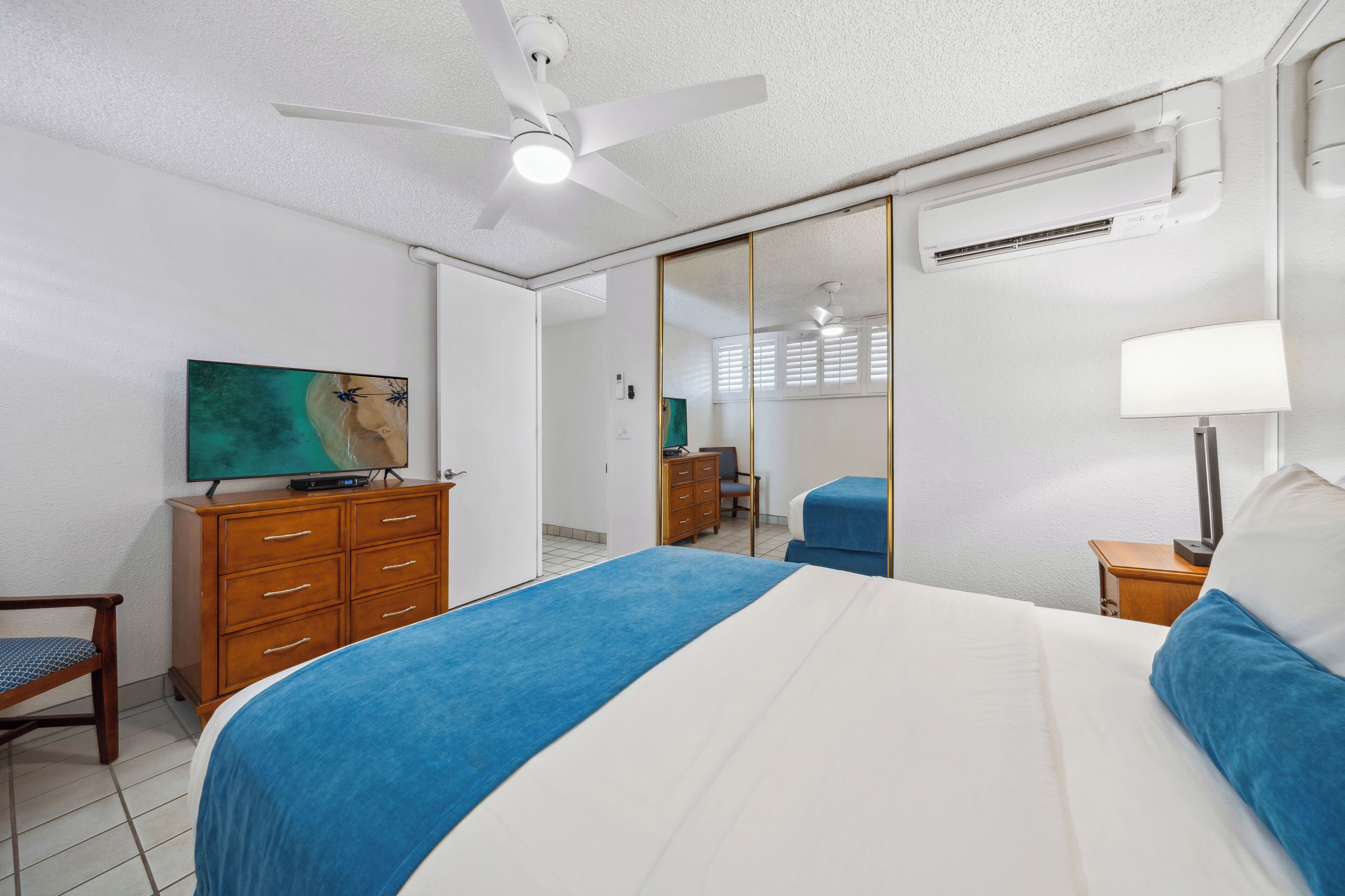 A bedroom with a bed, a ceiling fan, a TV, a dresser, and a mirror.