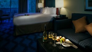 A hotel room with a bed, a sofa, a table with a bottle, glasses, and a fruit basket.