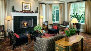 A traditional living room with a fireplace, patterned furniture, and large windows with curtains.