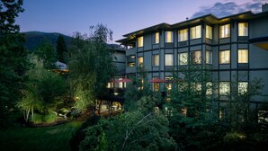 A multi-story hotel with a balcony and outdoor seating area, surrounded by lush greenery and a mountainous backdrop.