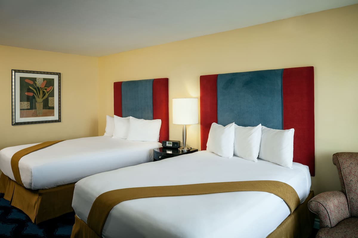 Een hotelkamer met twee bedden, een nachtkastje, een lamp, een stoel en een ingelijst schilderij aan de muur.