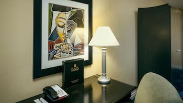 Una habitación de hotel con una obra de arte enmarcada en la pared, un escritorio con una lámpara, un teléfono y una silla de cuero negro.
