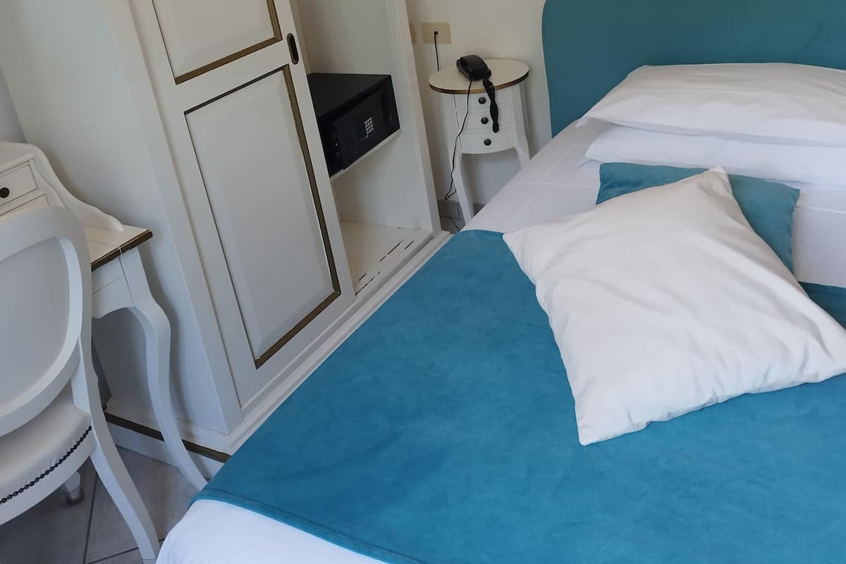 Hotellihuone, jossa on sänky, työpöytä, vaatekaappi ja yöpöytä, jossa on lamppu.
