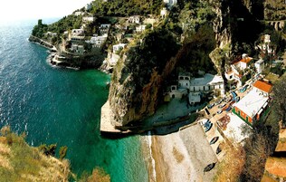 Un pueblo costero con edificios encaramados a acantilados, con vistas a aguas turquesas.