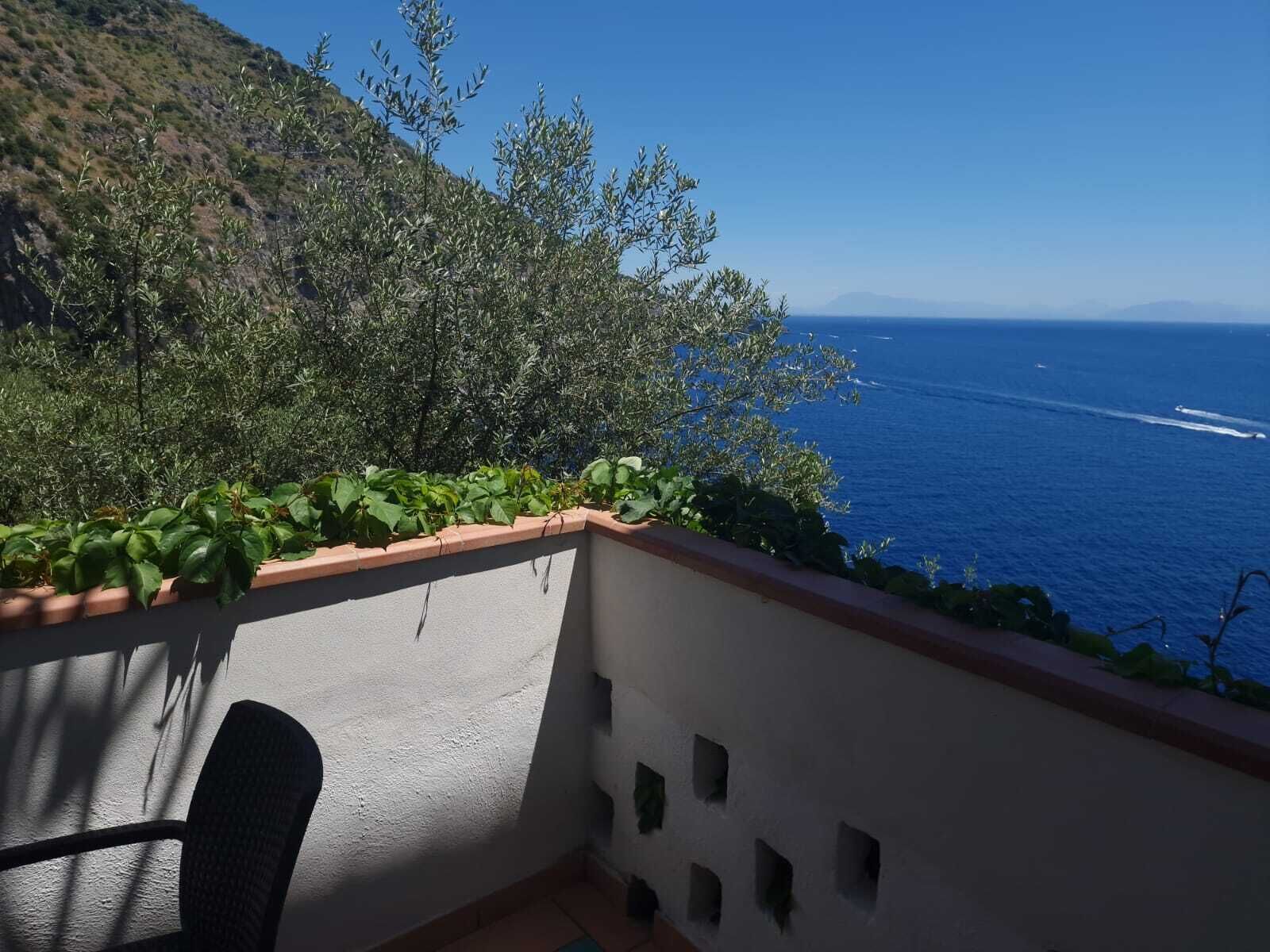 A balcony with a view of the sea and a hillside.
