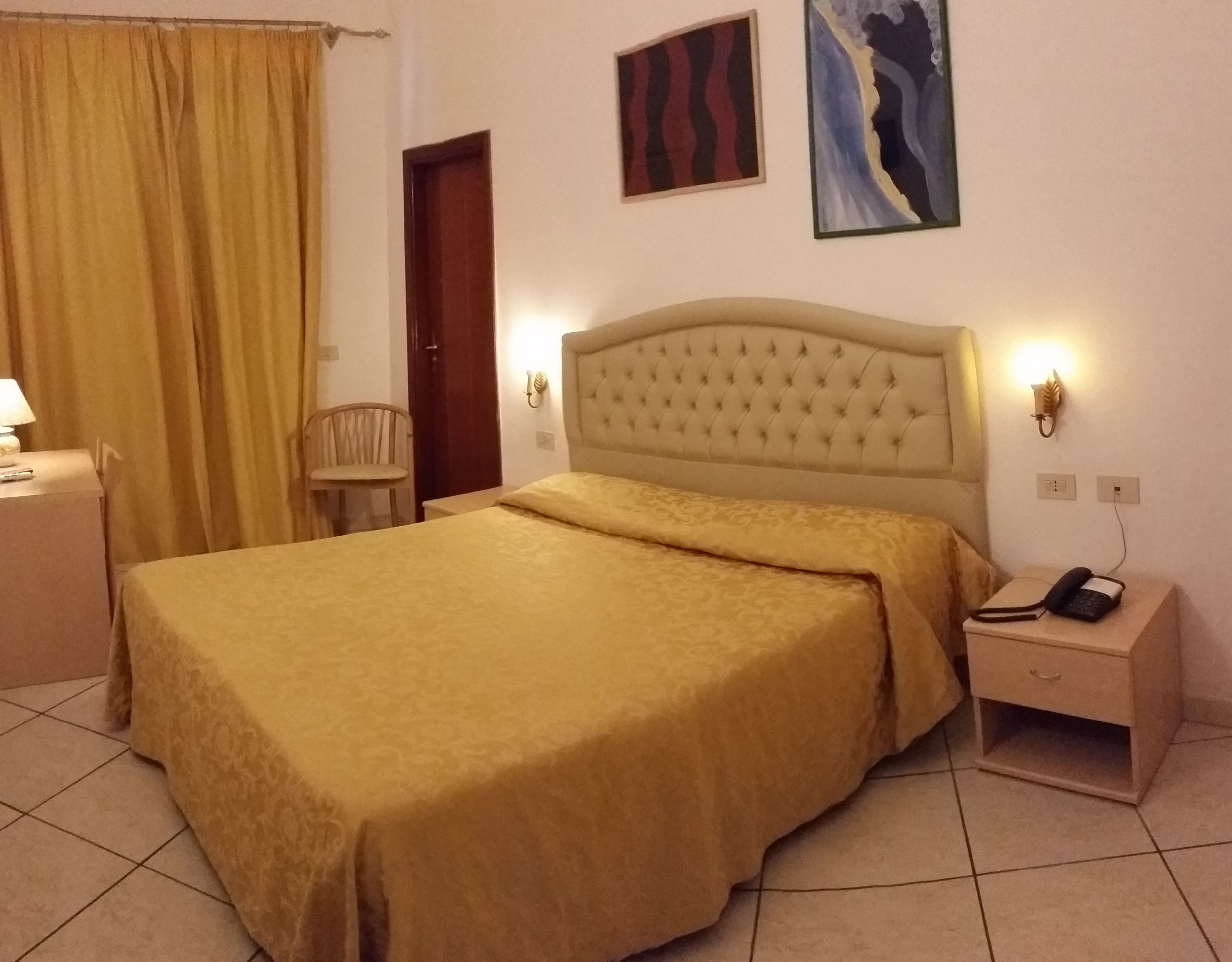 Habitación de hotel con una cama grande, una mesita de noche con lámpara, una silla y una obra de arte en la pared.