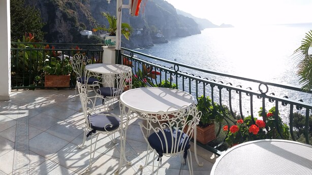 Un balcón con mobiliario exterior, vista al mar y un paisaje montañoso.