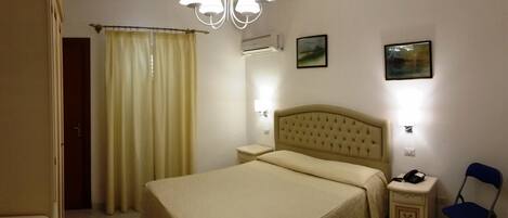 A hotel room with a bed, bedside tables, a chair, a curtain, and a chandelier.