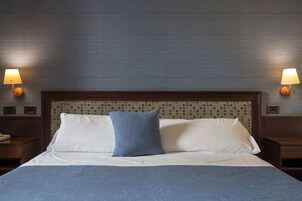 Una camera d'albergo con un letto grande, due comodini, una lampada a parete e una testiera a motivi decorativi.