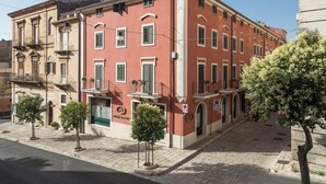 A red building with multiple windows and balconies, a green door, and small trees in front. - Hotel Montreal (Ragusa)