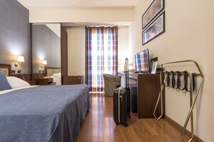 Una habitación de hotel con cama, escritorio, silla y maleta.