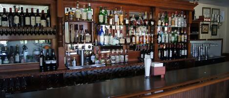 Un bar avec un comptoir en bois et des étagères remplies de différentes bouteilles d’alcool.