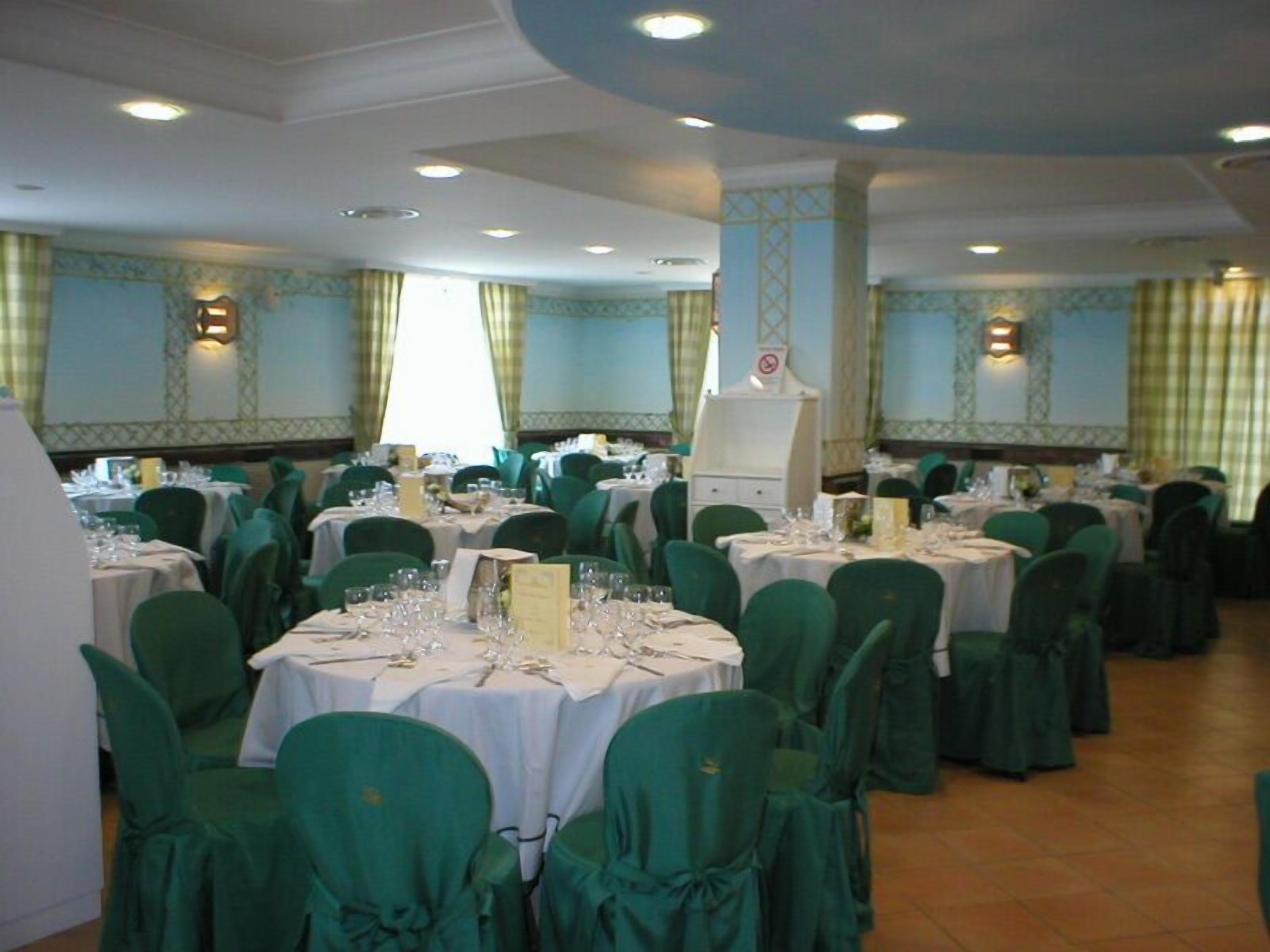A banquet hall with round tables, green chairs, and white tablecloths.