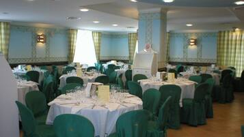 A banquet hall with round tables, green chairs, and white tablecloths.
