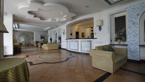 Un hall d’entrée spacieux doté d’un plafond incurvé, un espace central avec des canapés, un sol carrelé et un bar avec un comptoir et des éléments décoratifs.