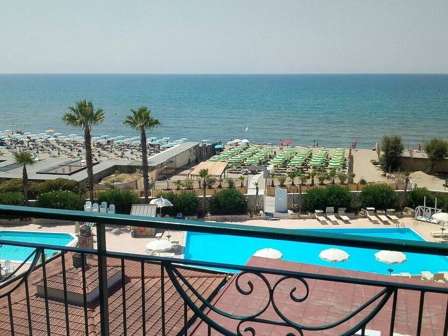A pool area with a view of the sea, surrounded by umbrellas and lounge chairs.