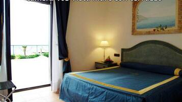 Habitación de hotel con cama, mesita de noche, lámpara, un cuadro y vista al mar a través de una ventana.